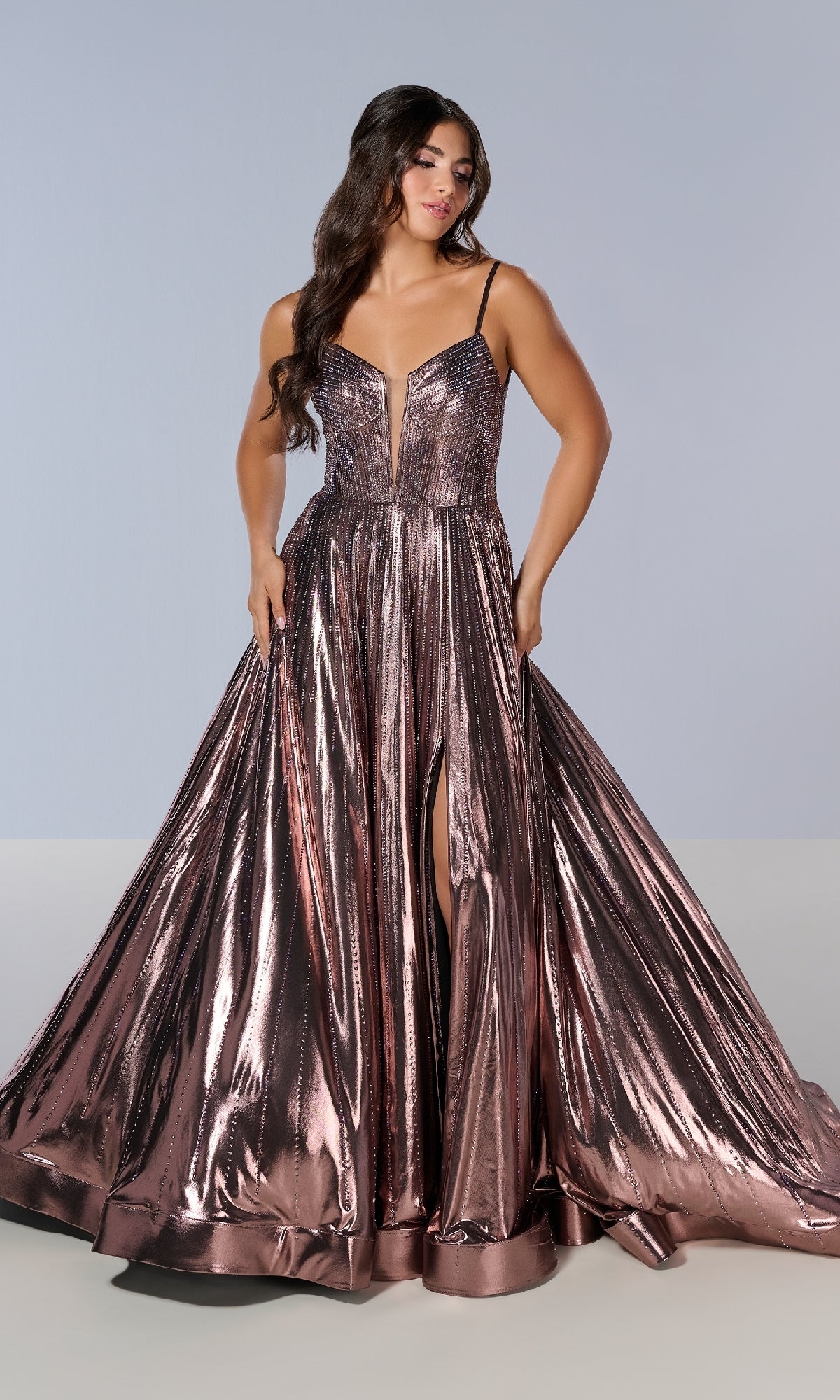 A woman models the Tiffany 16189 long prom dress in rose gold, featuring metallic pleats, a deep V-neckline, thin straps, and a high front slit against a plain light background.